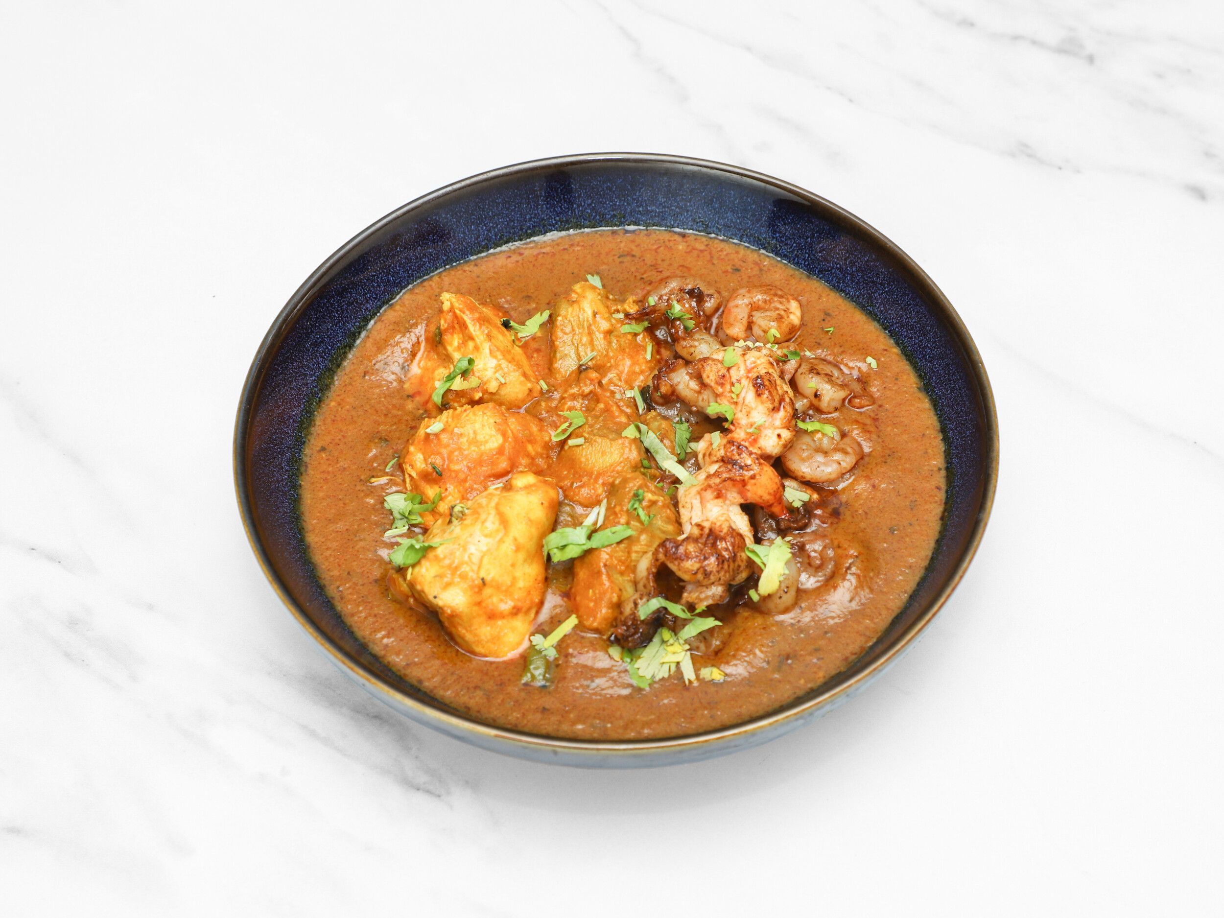 Chicken and king prawn curry in a dark blue bowl, garnished with fresh cilantro.