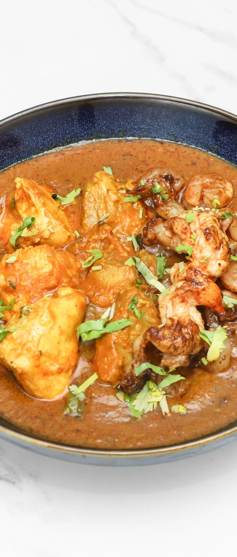Chicken and king prawn curry in a dark blue bowl, garnished with fresh cilantro.