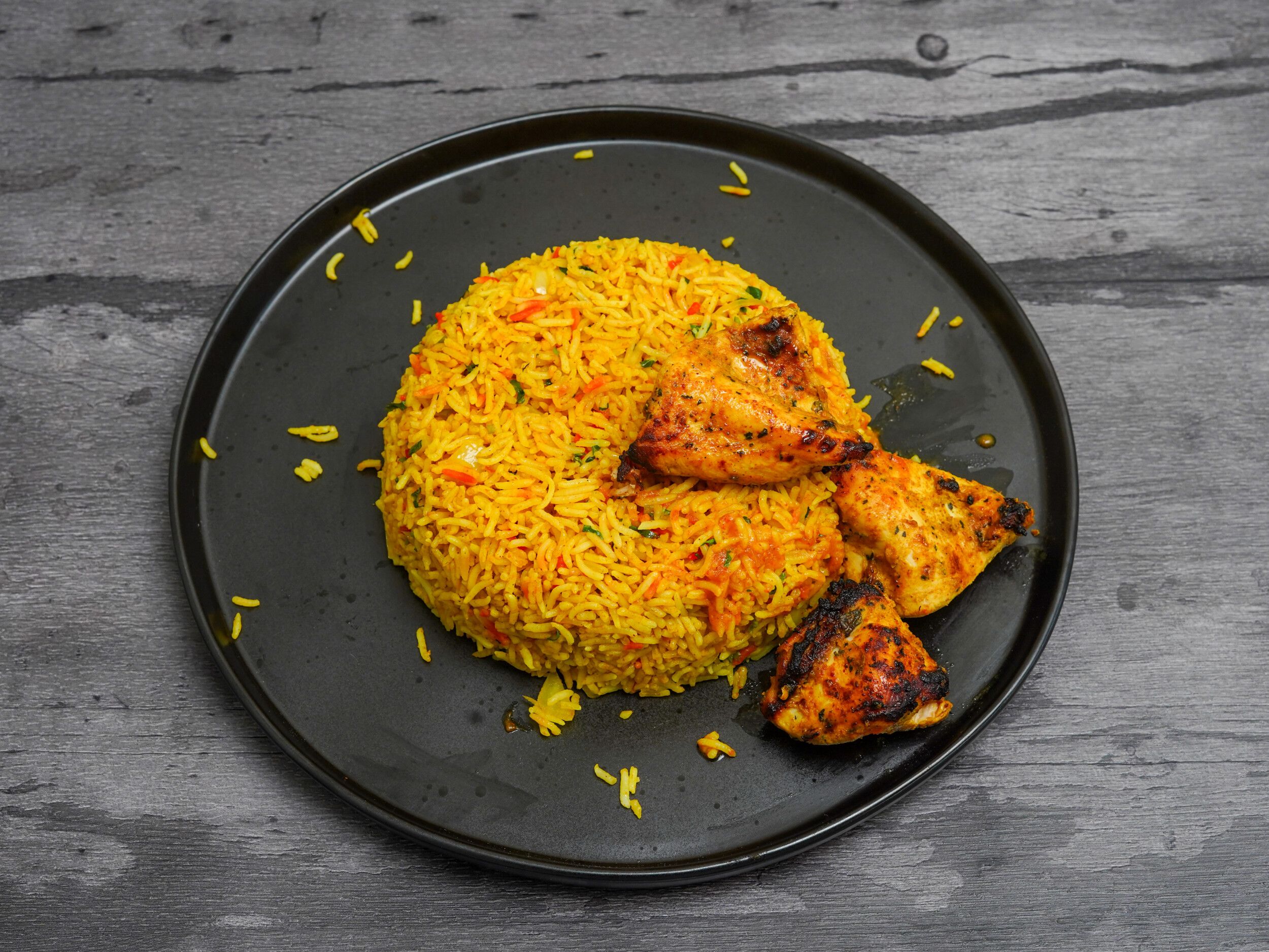 Saffron yellow rice with red and green garnishes, surrounded by three pieces of grilled chicken tikka