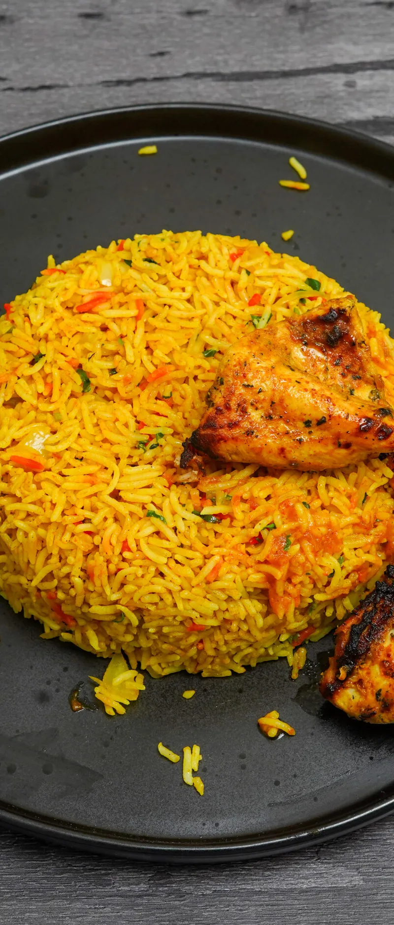 Saffron yellow rice with red and green garnishes, surrounded by three pieces of grilled chicken tikka