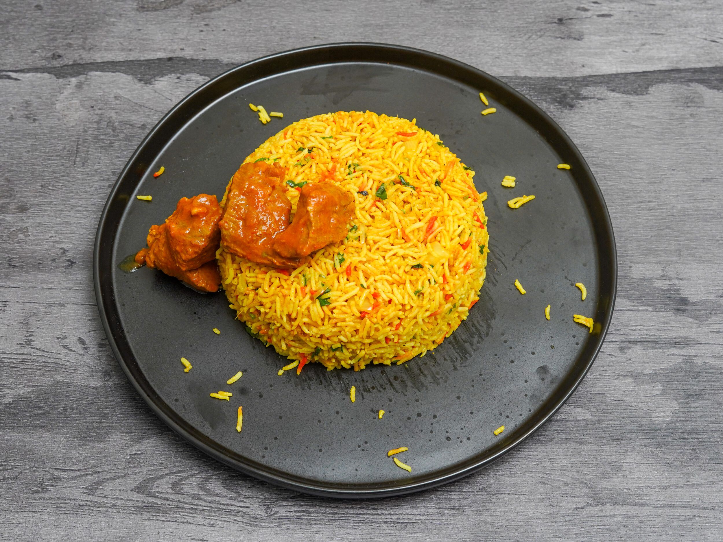 Chicken biryani with vibrant orange rice and pieces of chicken curry on a black serving plate.