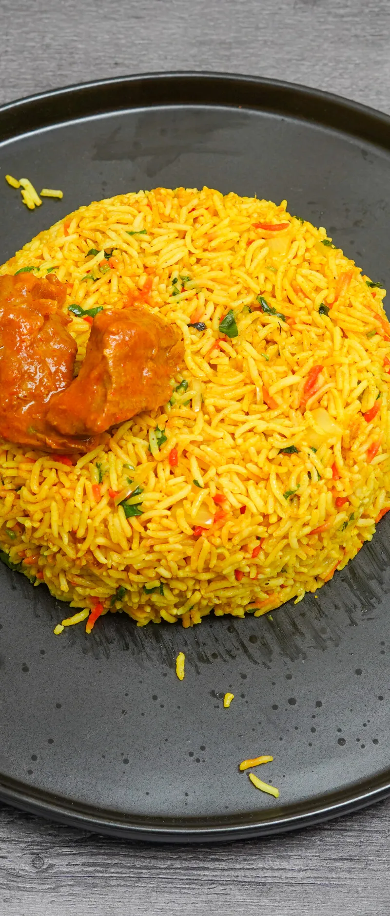 Chicken biryani with vibrant orange rice and pieces of chicken curry on a black serving plate.