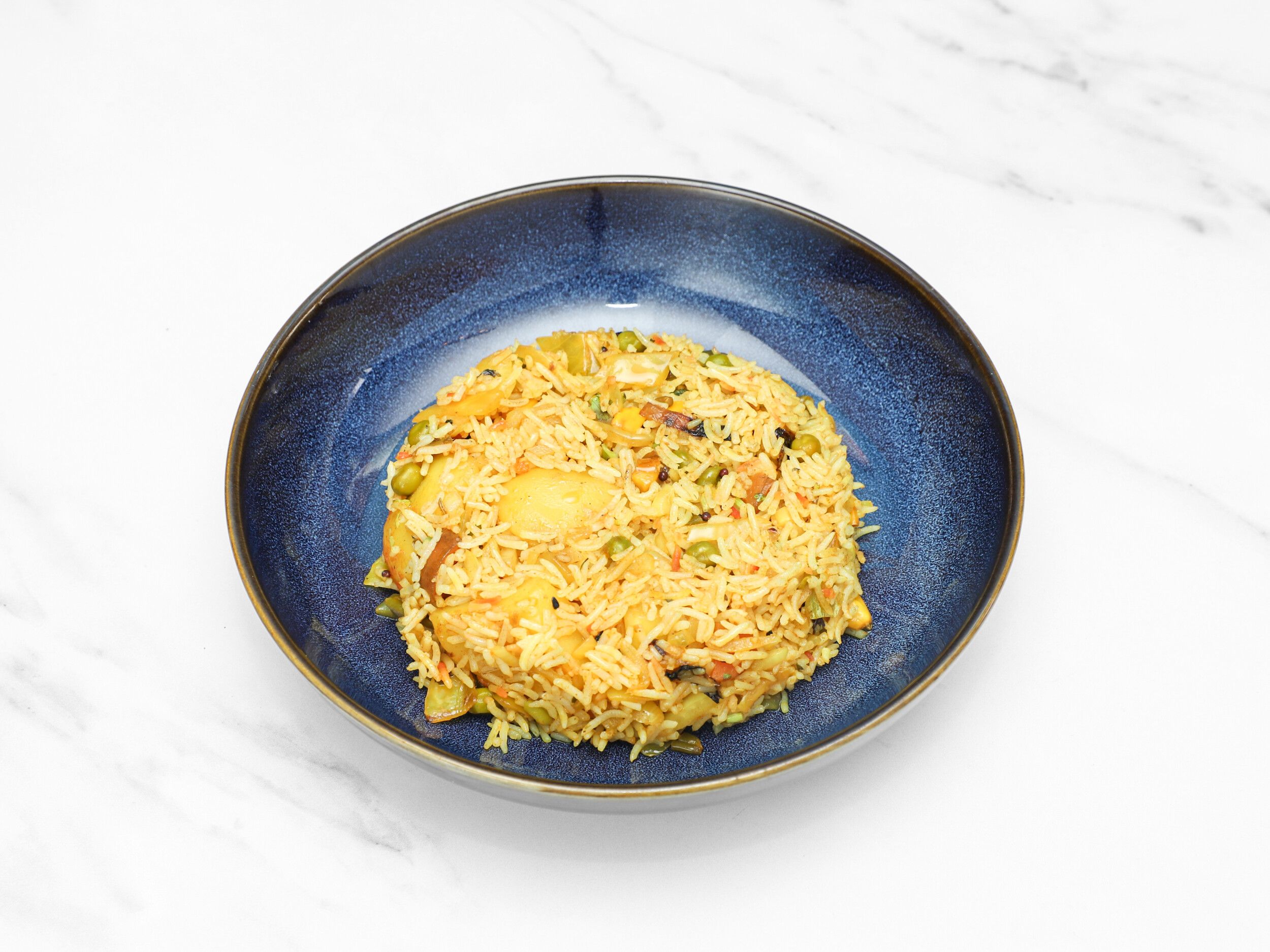 A mound of fluffy yellow pilau rice with mixed vegetables in a deep blue ceramic bowl.