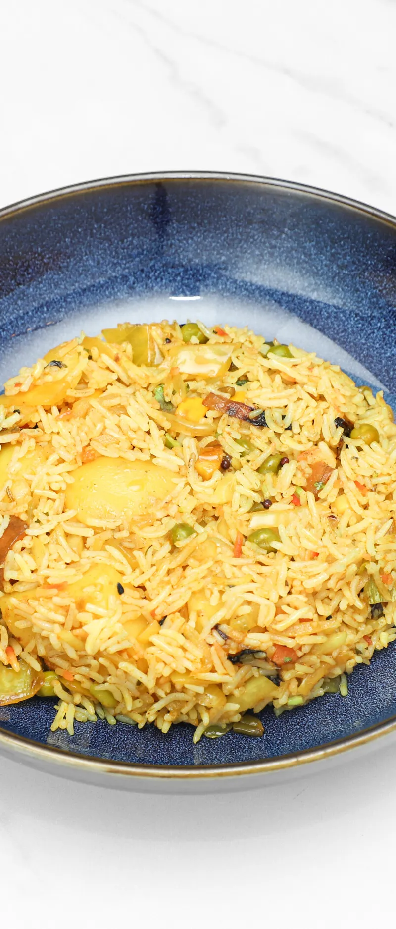 A mound of fluffy yellow pilau rice with mixed vegetables in a deep blue ceramic bowl.