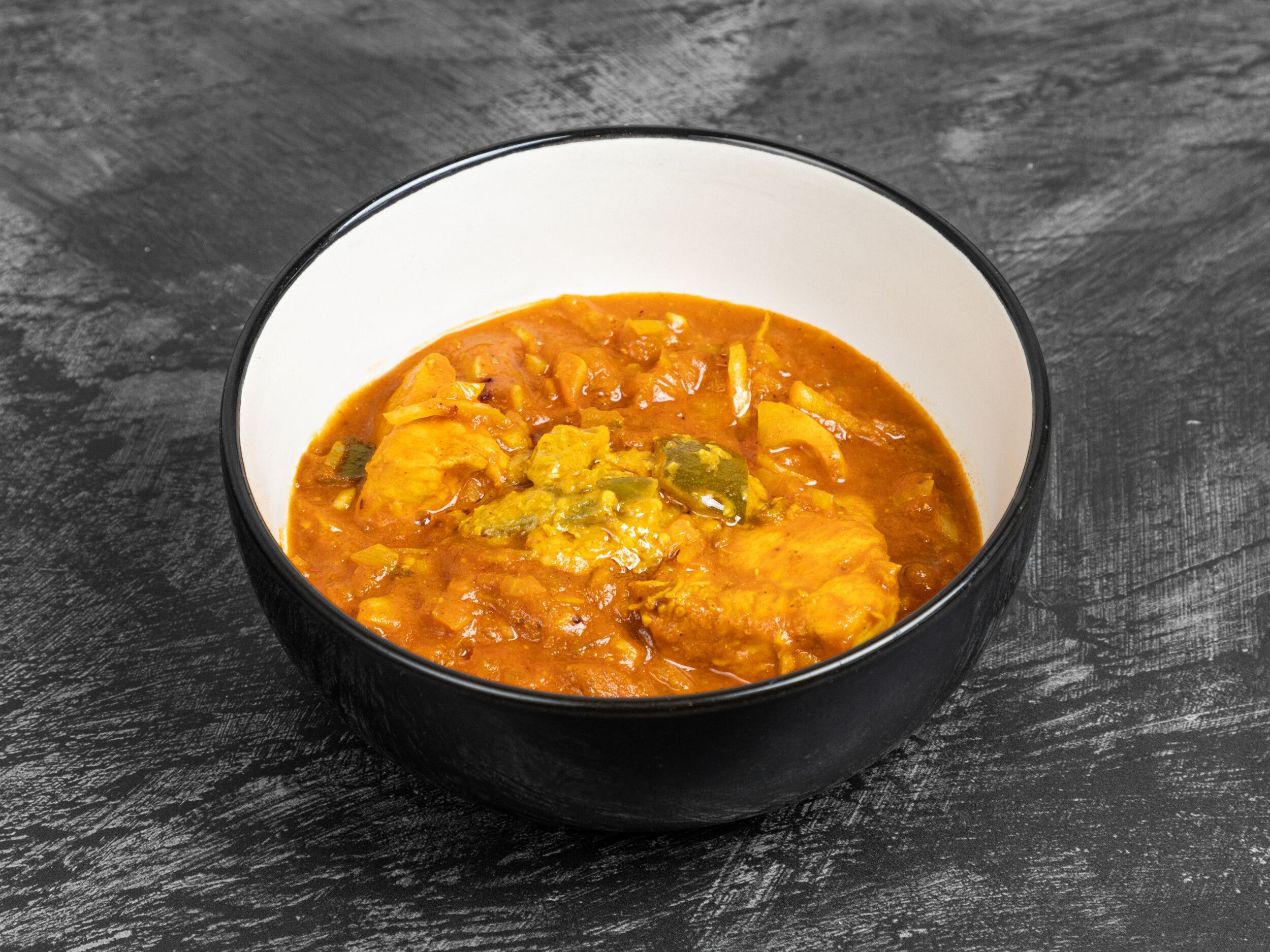 Orange chicken curry with bell peppers and onions in a white and black serving bowl.