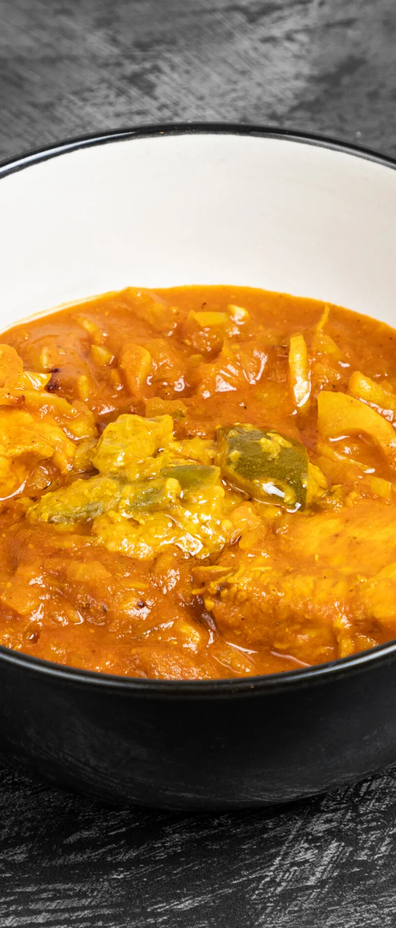 Orange chicken curry with bell peppers and onions in a white and black serving bowl.