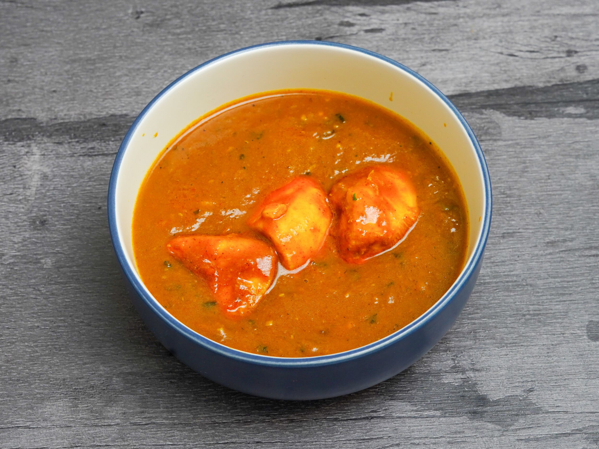 Chicken tikka pieces in a vibrant orange curry sauce served in a blue bowl