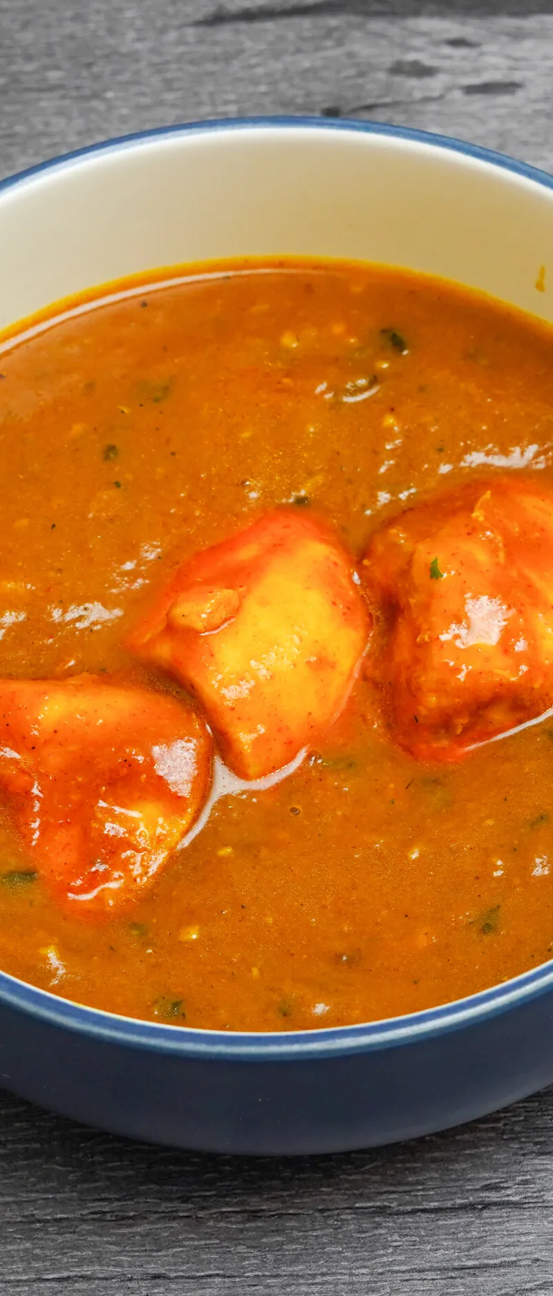 Chicken tikka pieces in a vibrant orange curry sauce served in a blue bowl
