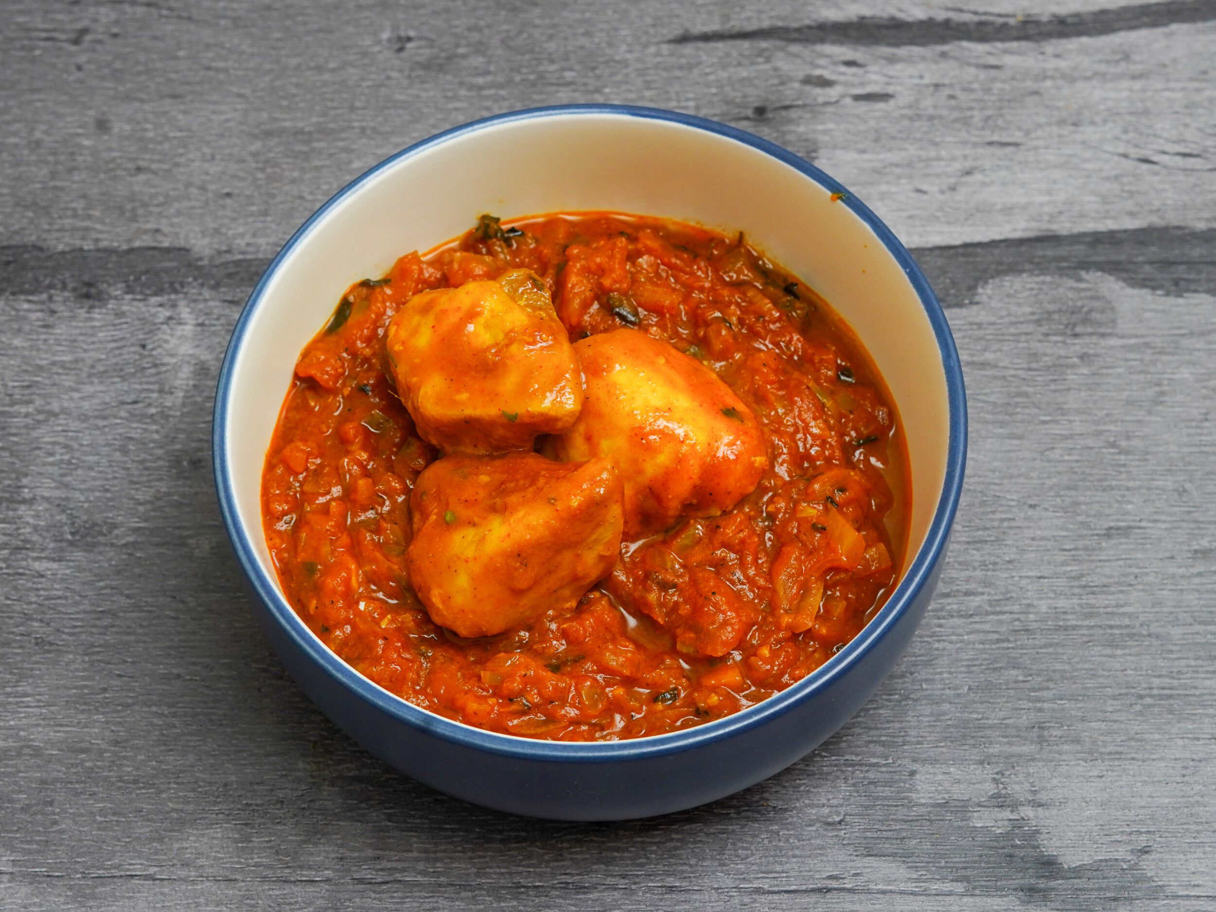 Chicken tikka masala with tender chicken pieces in a rich orange sauce, served in a blue bowl.
