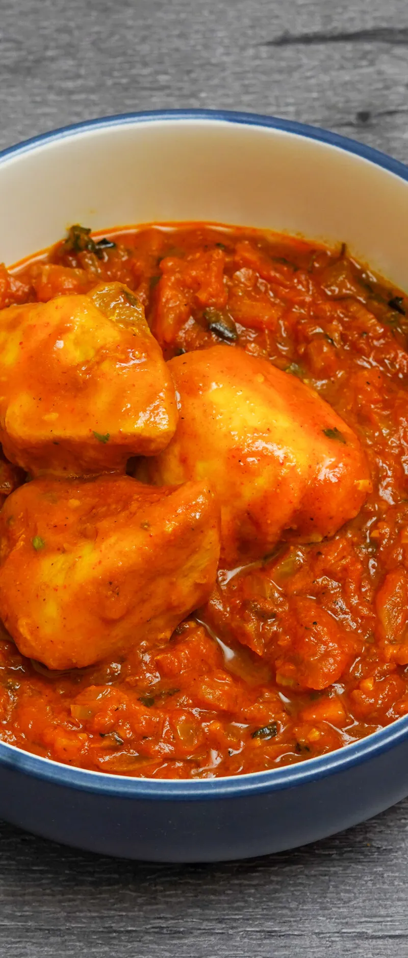 Chicken tikka masala with tender chicken pieces in a rich orange sauce, served in a blue bowl.