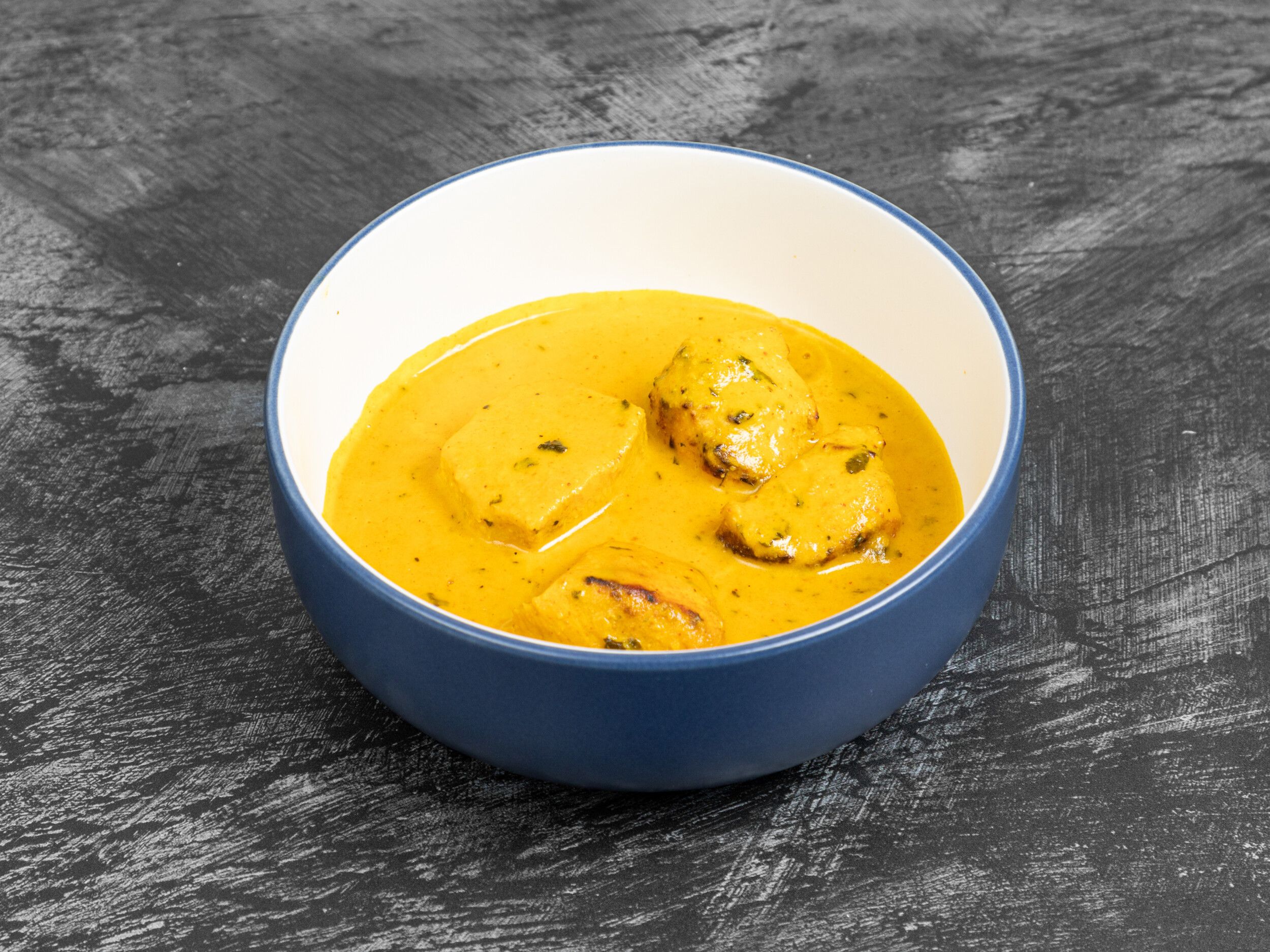 Malai Kofta in a rich, creamy yellow curry sauce, served in a blue and white bowl