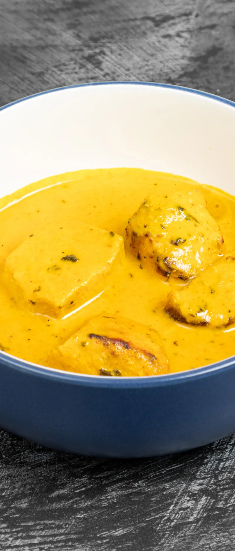 Malai Kofta in a rich, creamy yellow curry sauce, served in a blue and white bowl