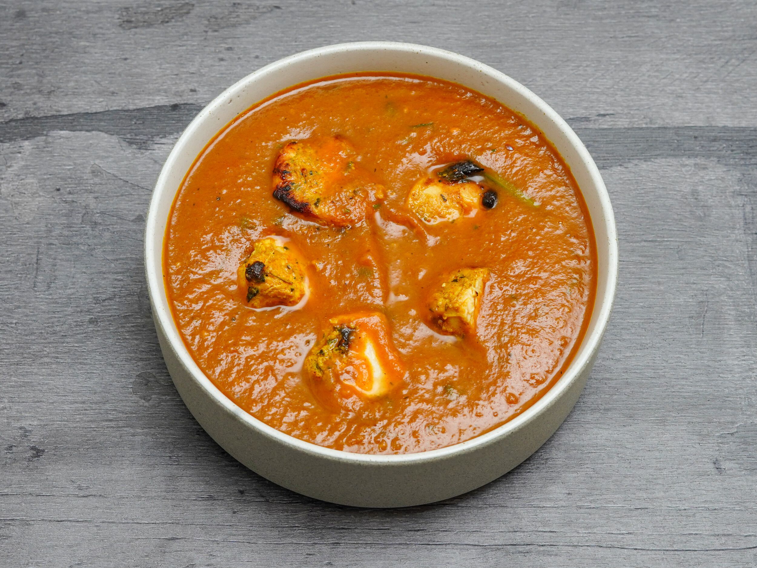 Round serving bowl of paneer tikka masala with grilled paneer cheese cubes in rich orange sauce.