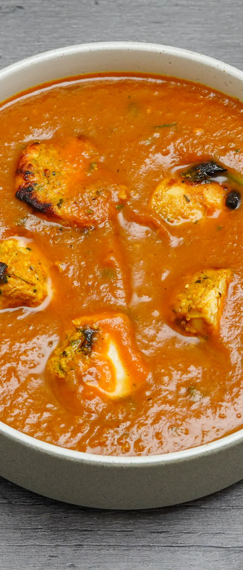 Round serving bowl of paneer tikka masala with grilled paneer cheese cubes in rich orange sauce.