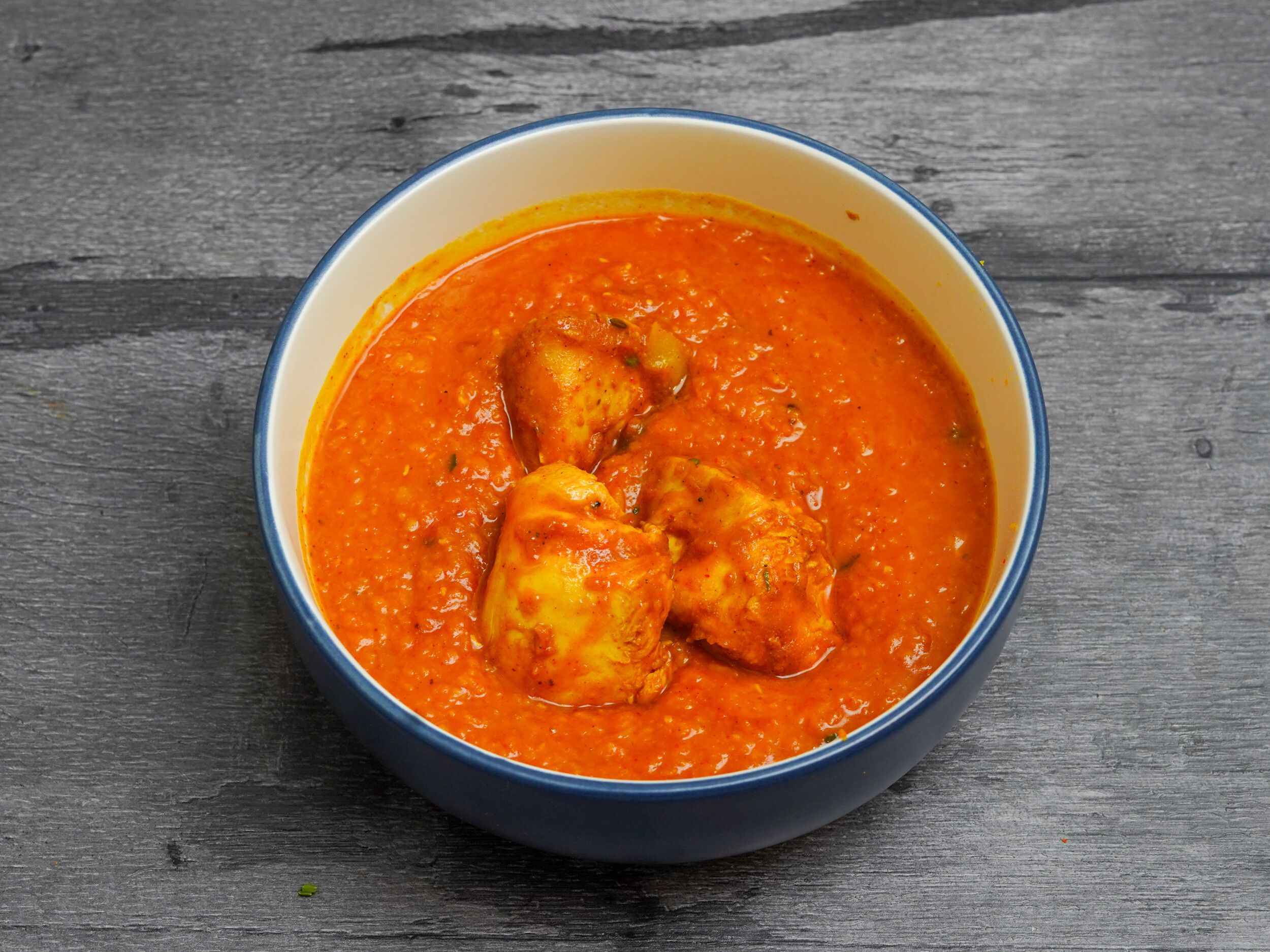Chicken curry with an orange-red sauce and three pieces of chicken in a white and blue bowl