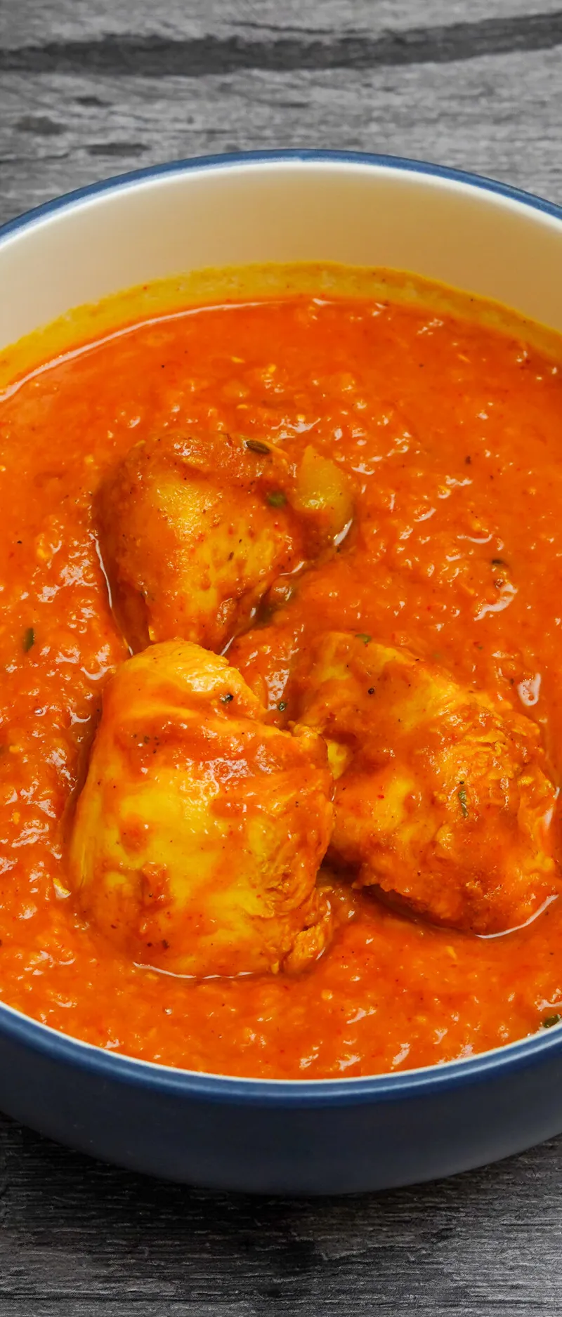 Chicken curry with an orange-red sauce and three pieces of chicken in a white and blue bowl