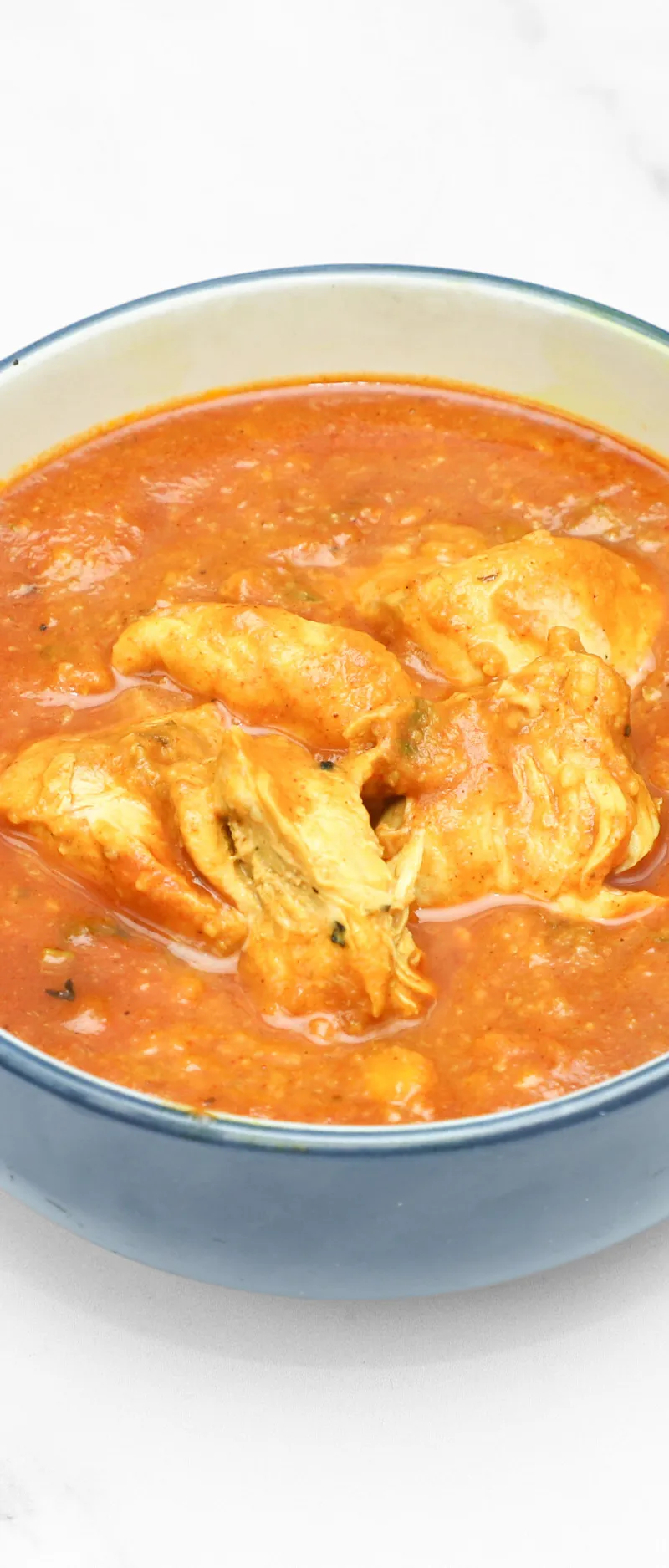 A blue bowl filled with chicken tikka masala on a white marble background.