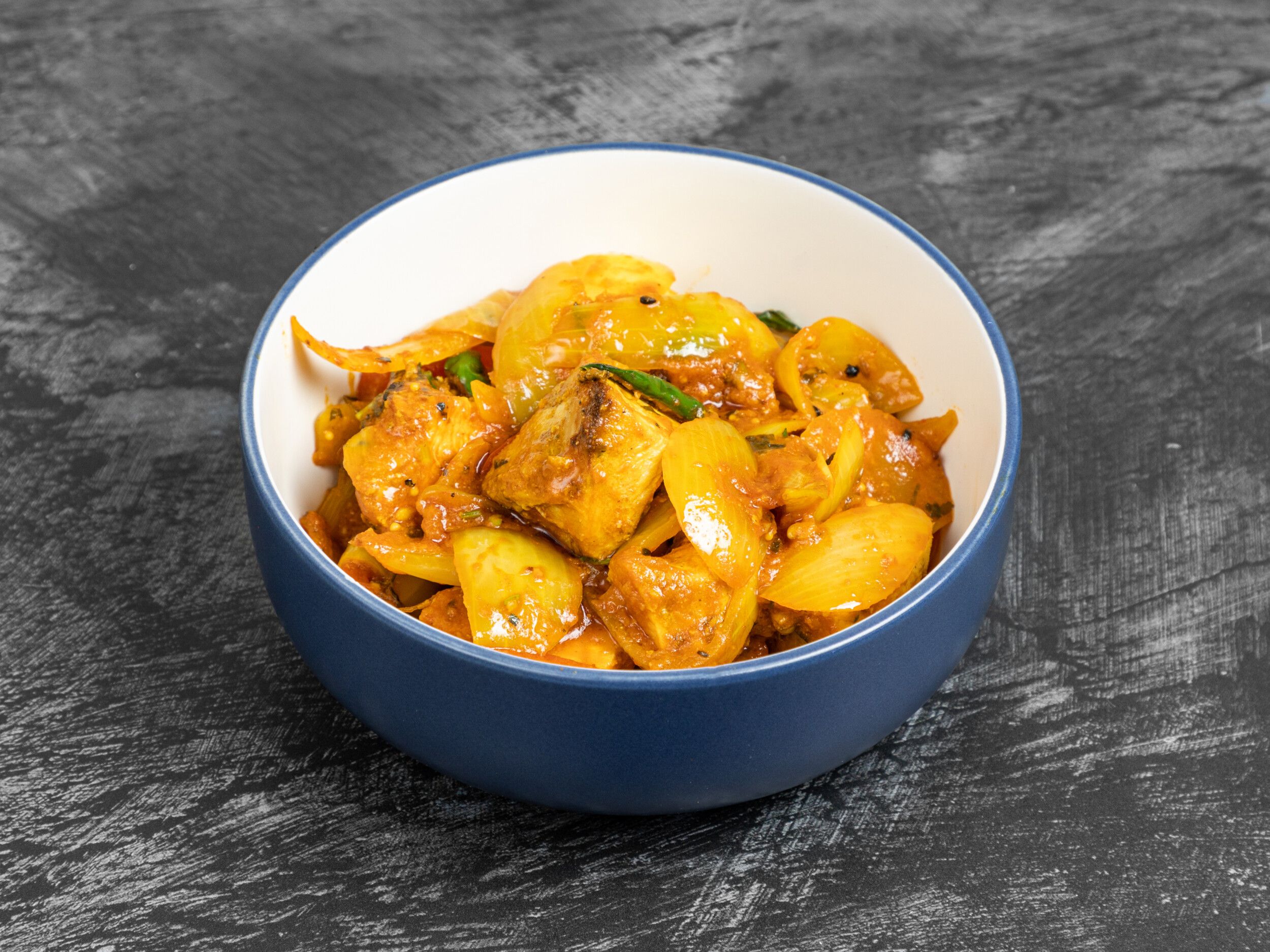 A close-up of a blue and white bowl filled with chilli chicken, onions, and green chillies.