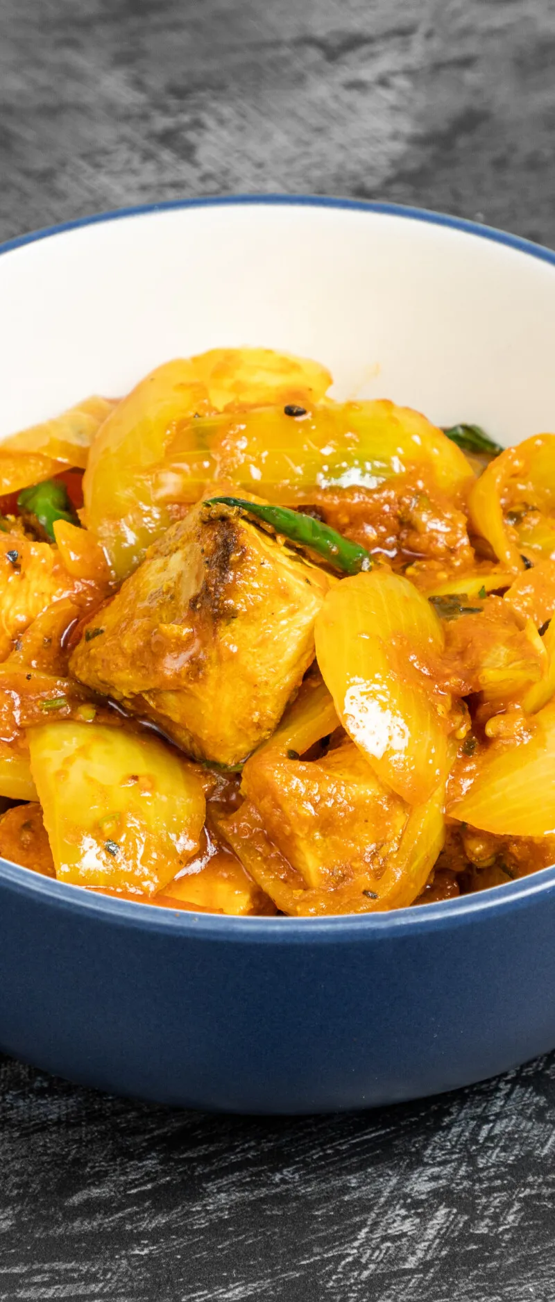 A close-up of a blue and white bowl filled with chilli chicken, onions, and green chillies.