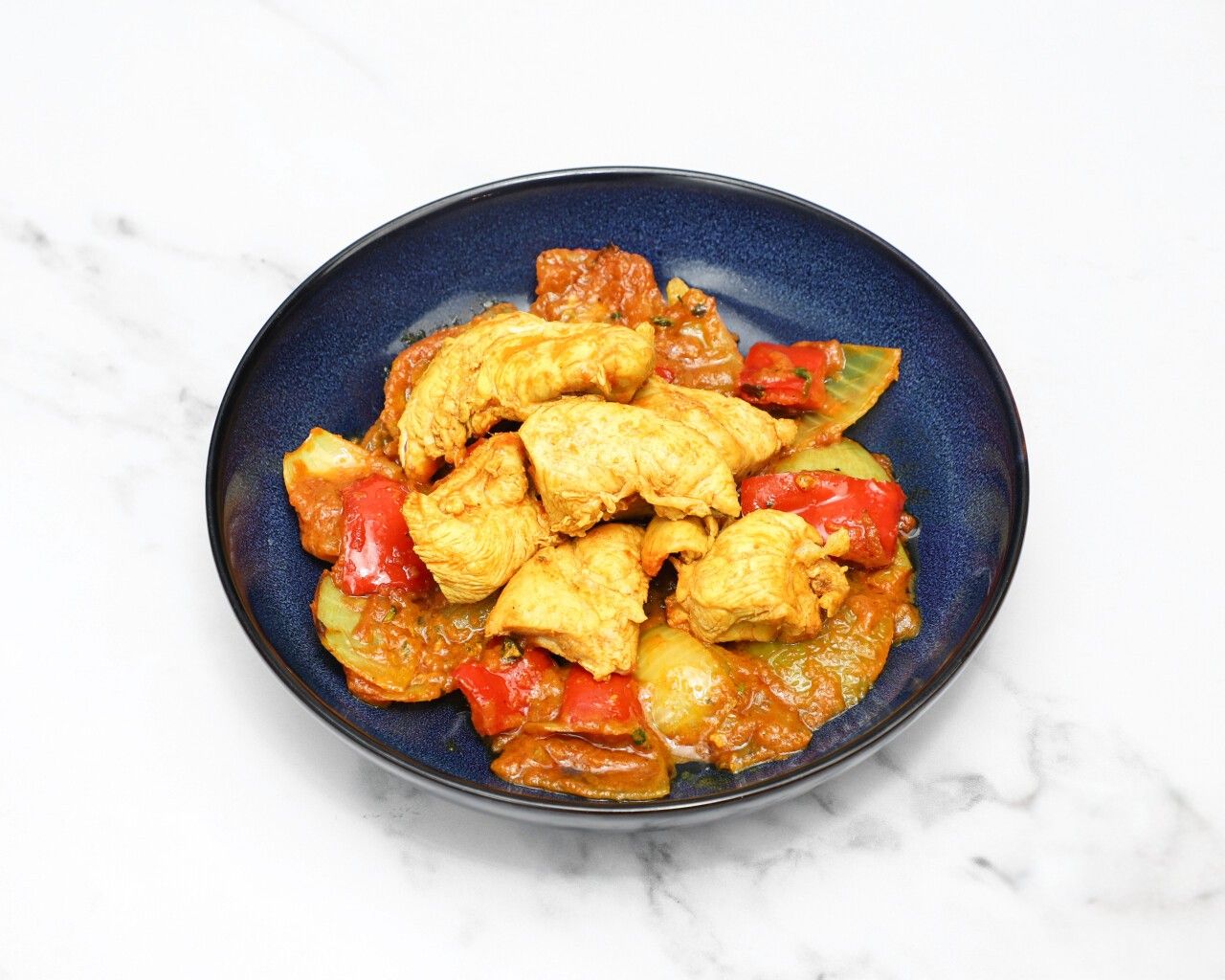 Chicken jalfrezi with chicken pieces, red peppers, and onions in a dark blue bowl.
