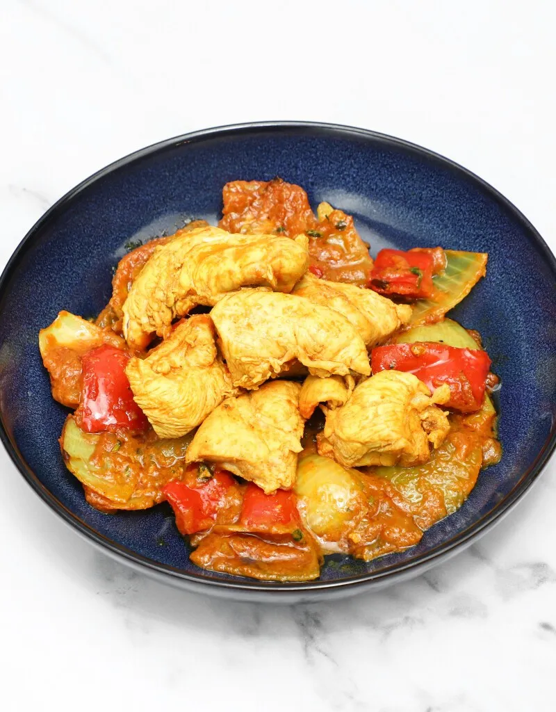 Chicken jalfrezi with chicken pieces, red peppers, and onions in a dark blue bowl.