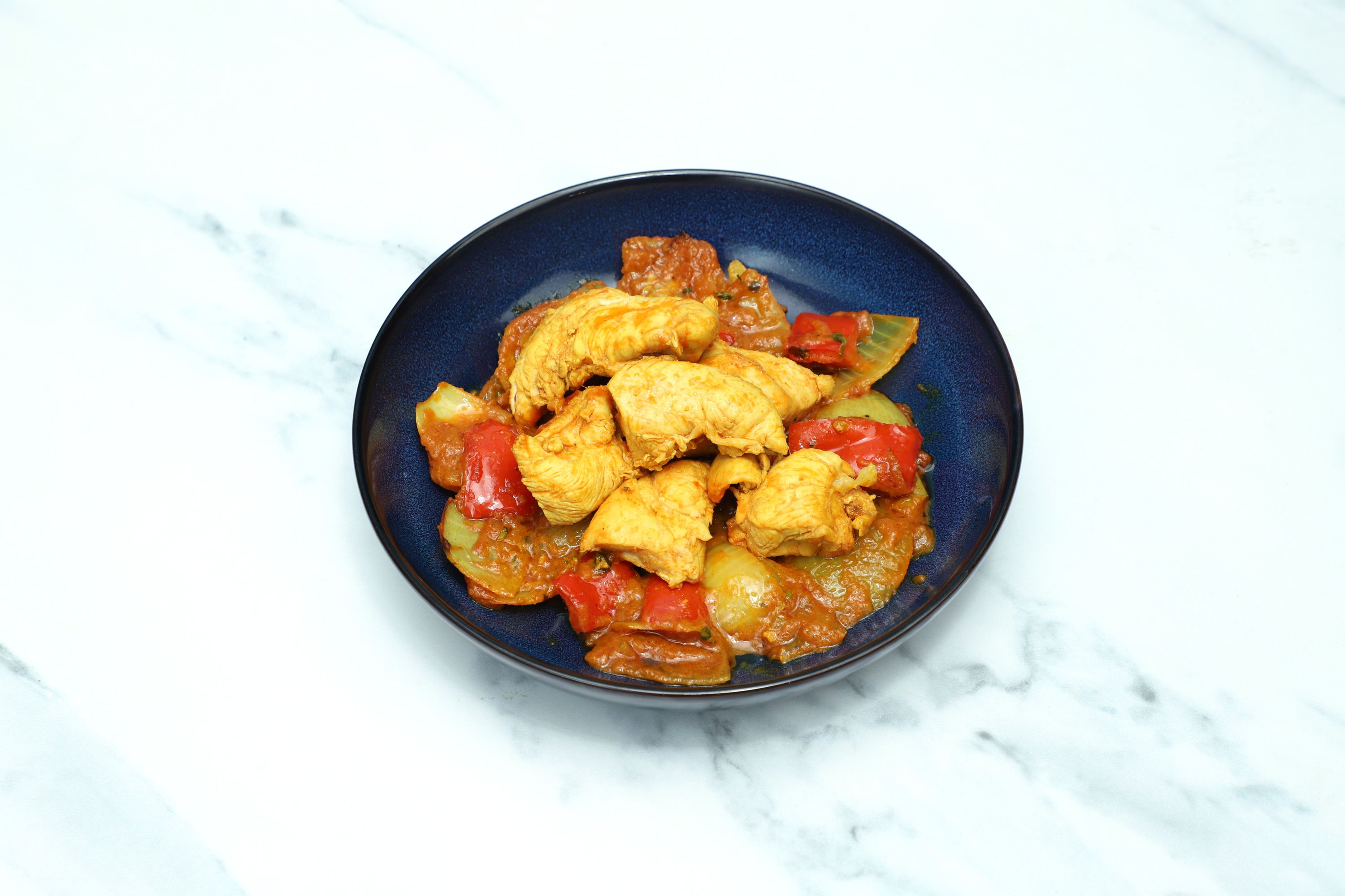 Chicken stir-fry with peppers and onions in a rich orange sauce, served in a dark blue bowl.