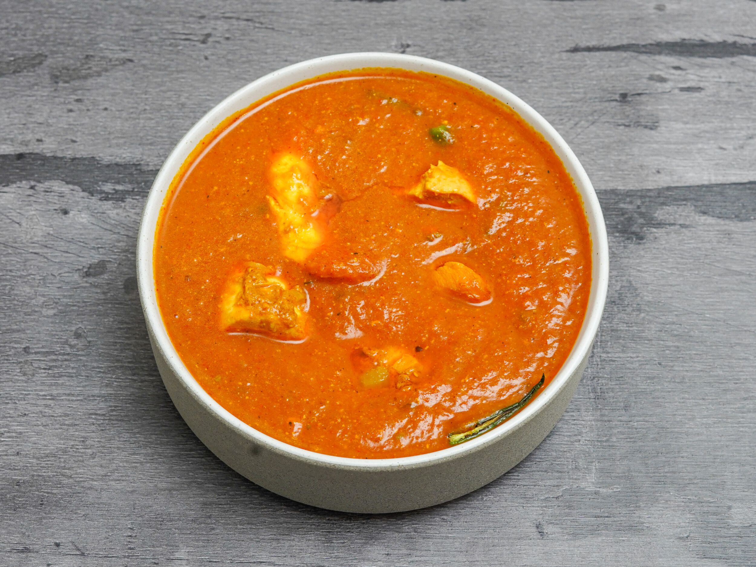 Chicken tikka masala curry in a white serving bowl with rich orange sauce and chicken pieces.