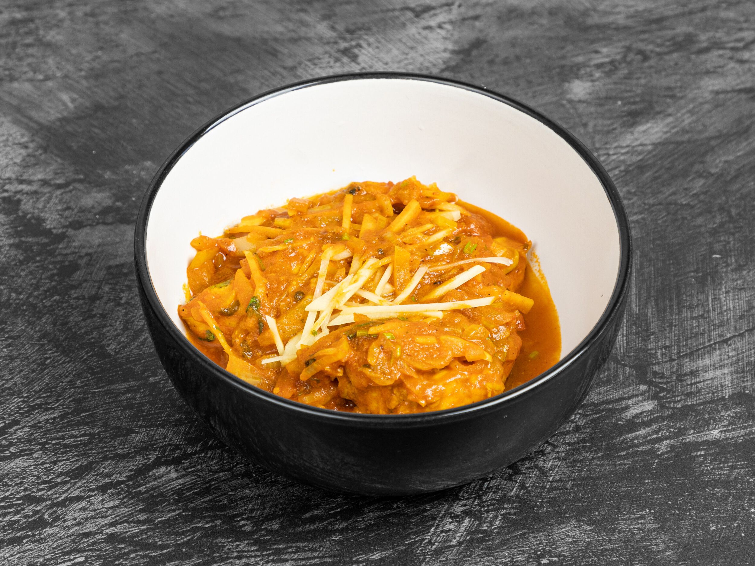 Chicken curry with an orange sauce, julienned ginger, and green herbs in a black bowl.