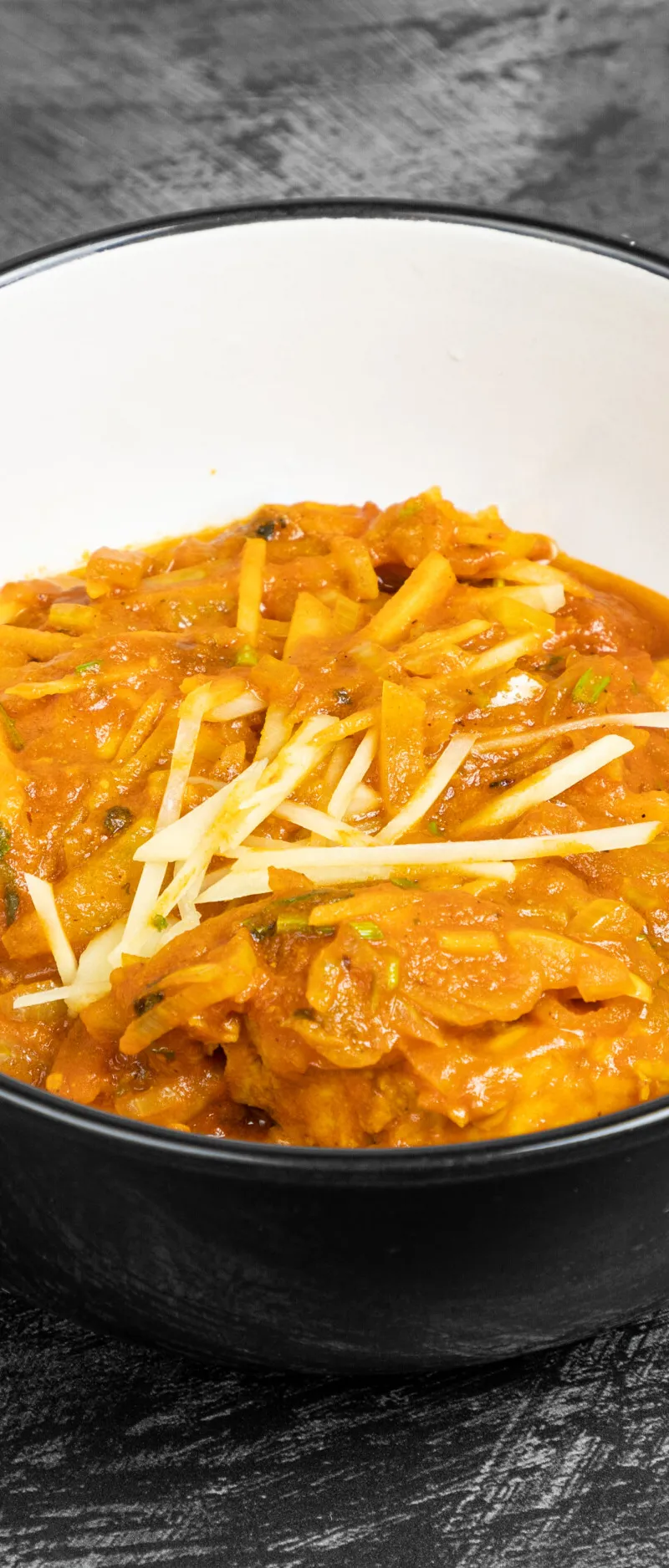 Chicken curry with an orange sauce, julienned ginger, and green herbs in a black bowl.