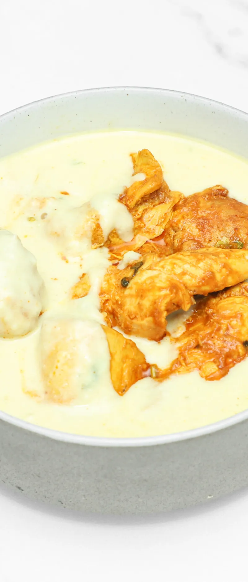 Creamy yellowish Malai chicken curry in a grey bowl on a white marble background