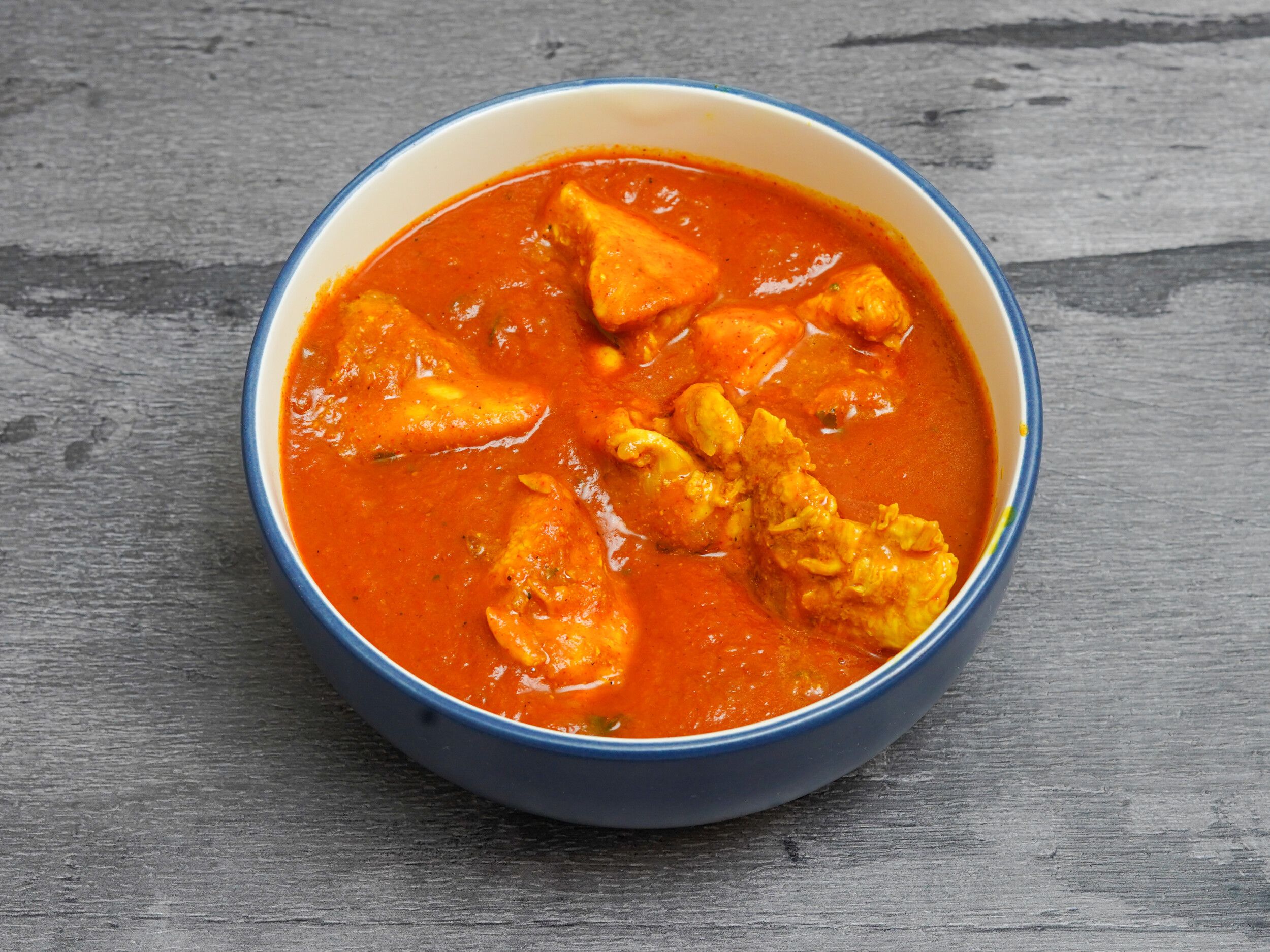 A blue and white bowl filled with a vibrant orange-red curry and chunks of chicken.