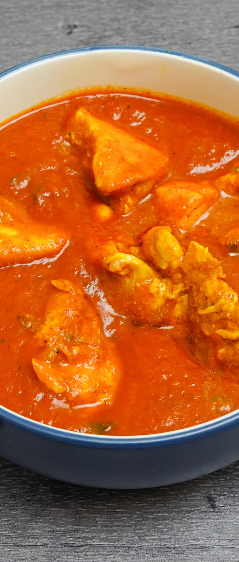 A blue and white bowl filled with a vibrant orange-red curry and chunks of chicken.