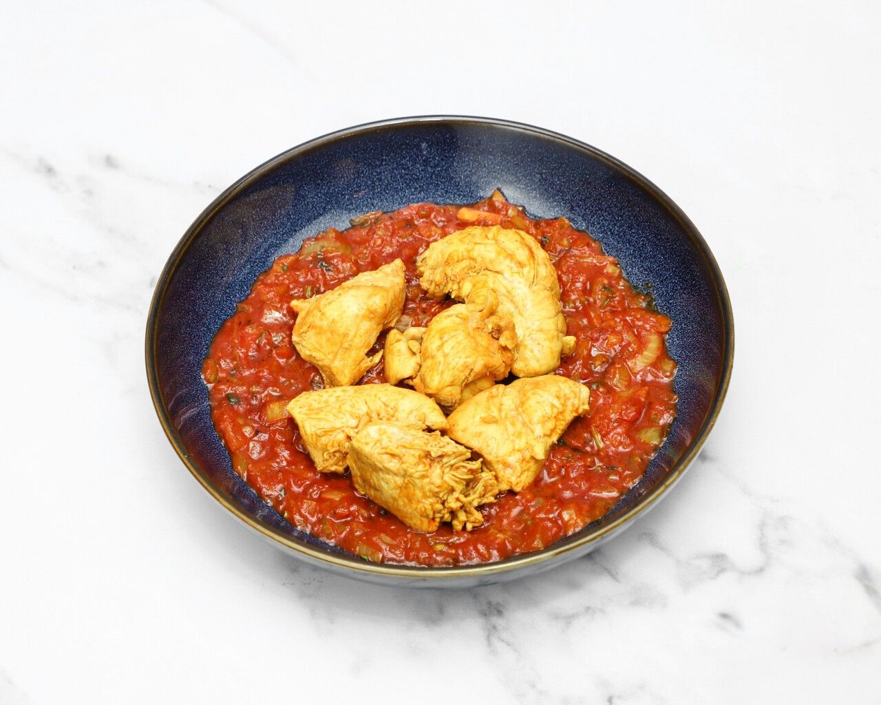 Golden-brown chicken breast pieces served in a blue bowl atop a vibrant red tomato sauce.