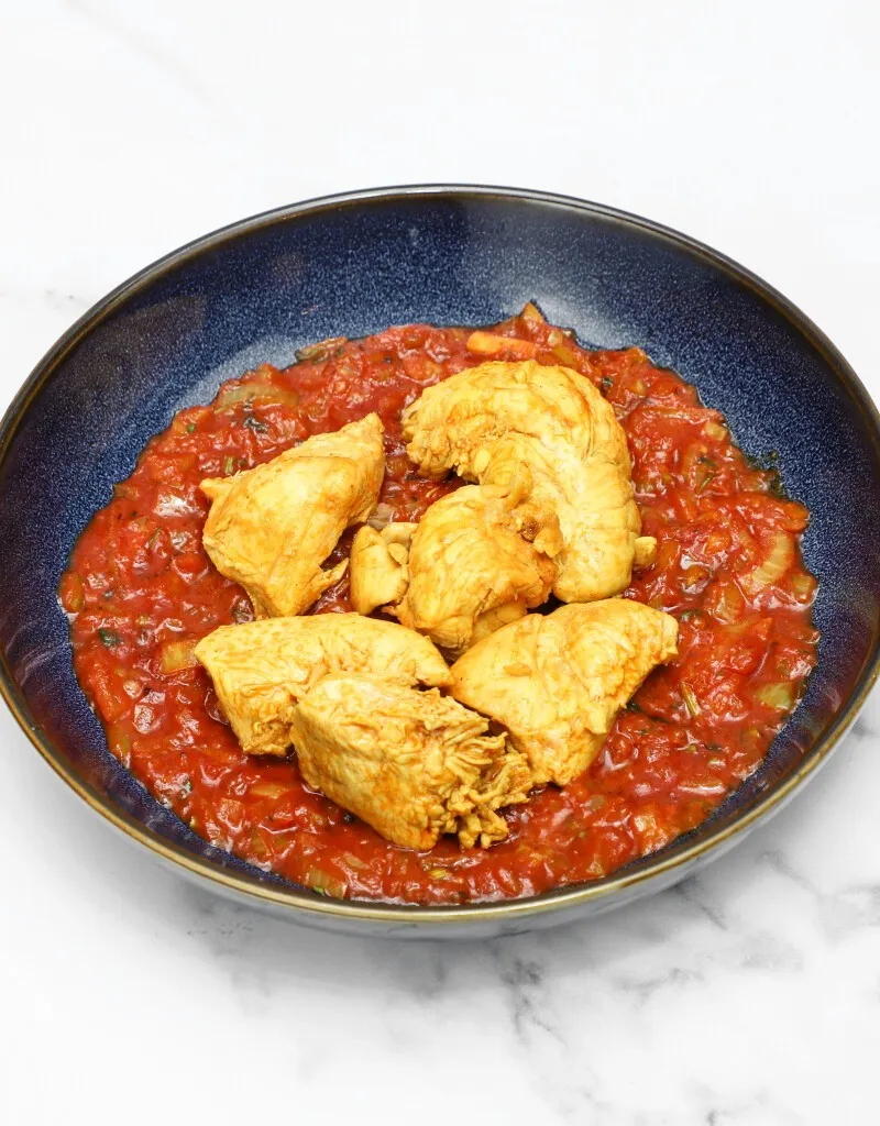 Golden-brown chicken breast pieces served in a blue bowl atop a vibrant red tomato sauce.