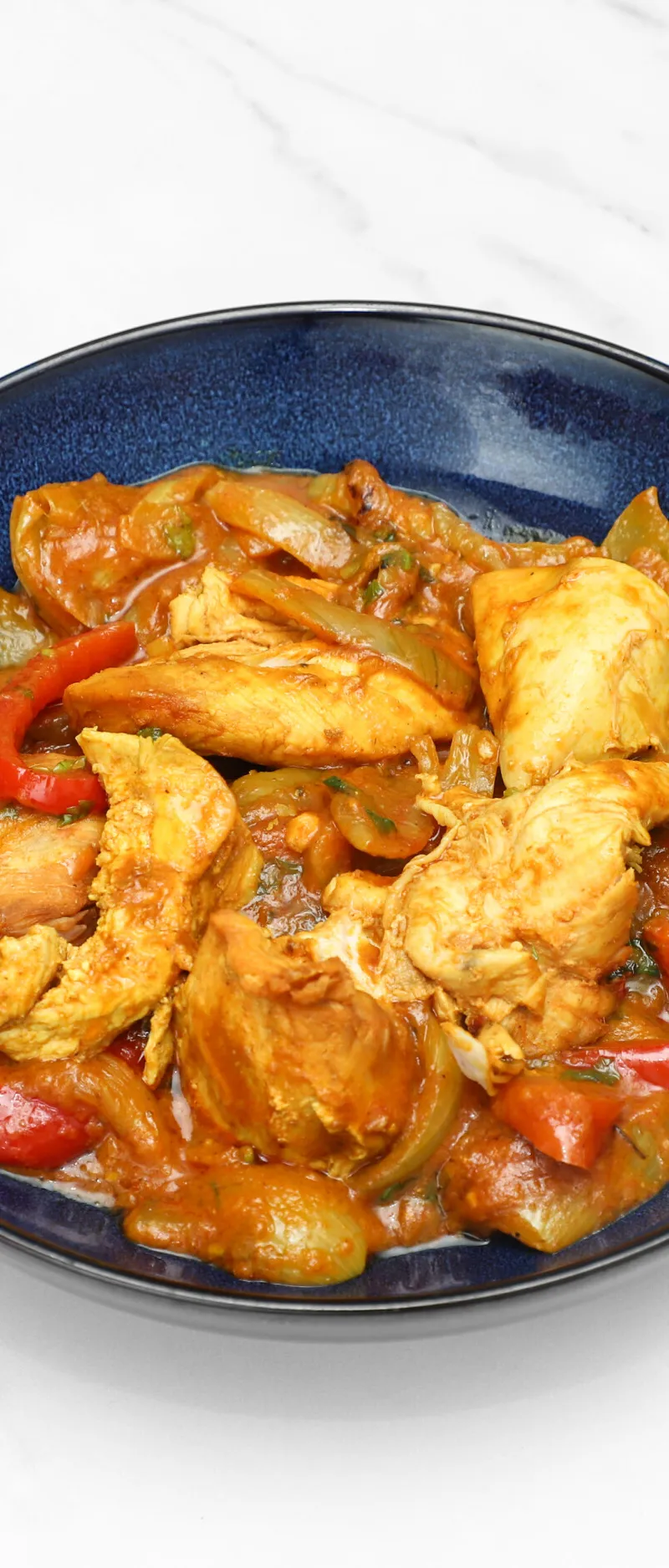 Chicken curry with large chunks of chicken, yellow onions, and red and green peppers in a rich sauce, served in a blue bowl.
