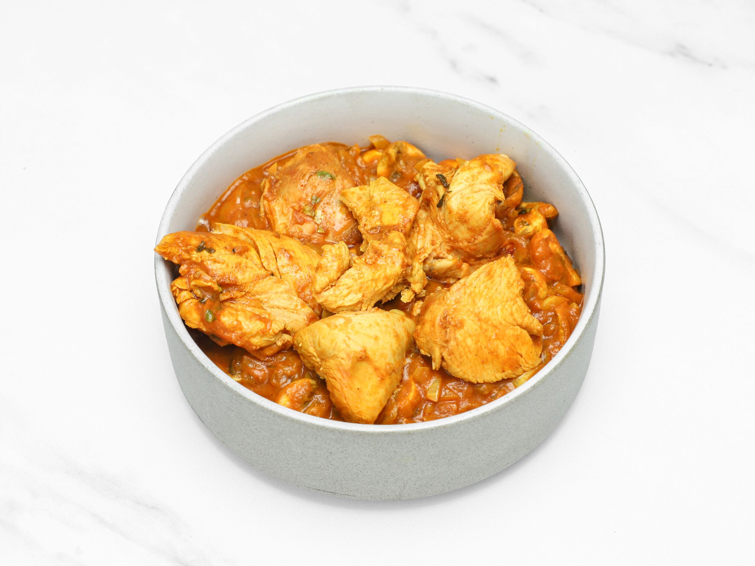 A grey bowl fills the frame, showcasing succulent pieces of chicken in a vibrant orange curry sauce.