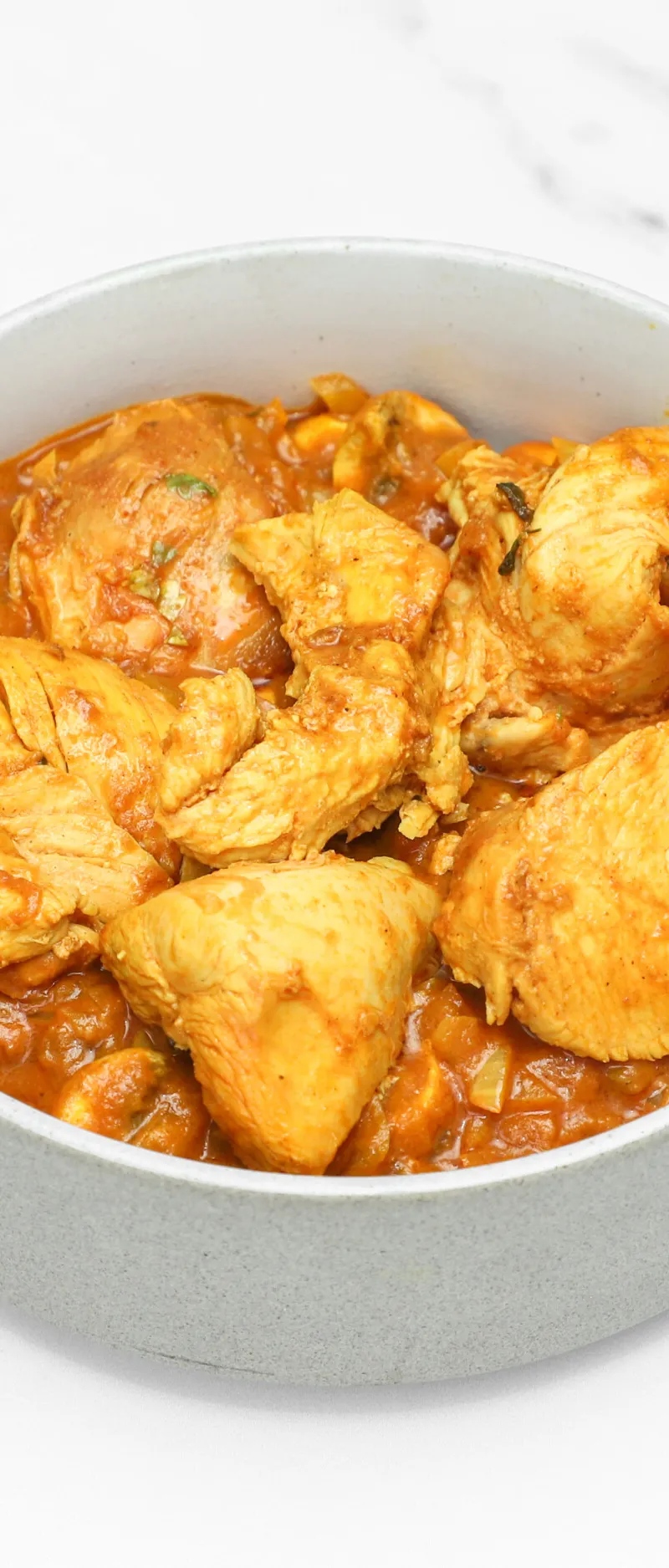 A grey bowl fills the frame, showcasing succulent pieces of chicken in a vibrant orange curry sauce.