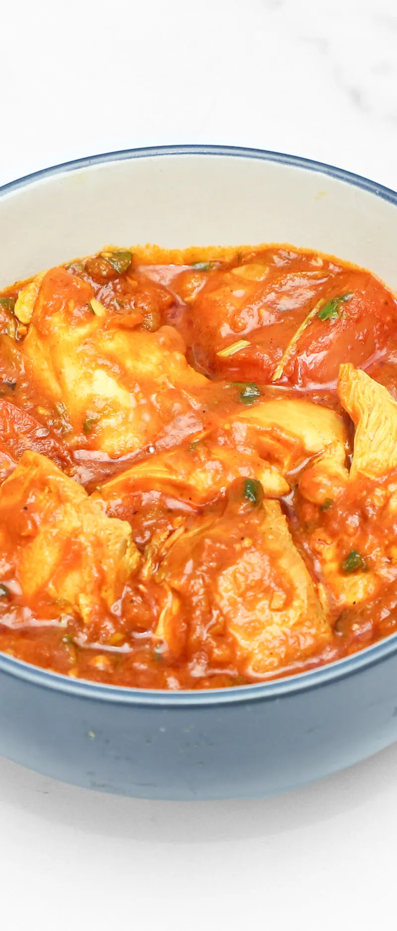 Chicken and tomato curry in a light blue ceramic bowl on a white marble surface.