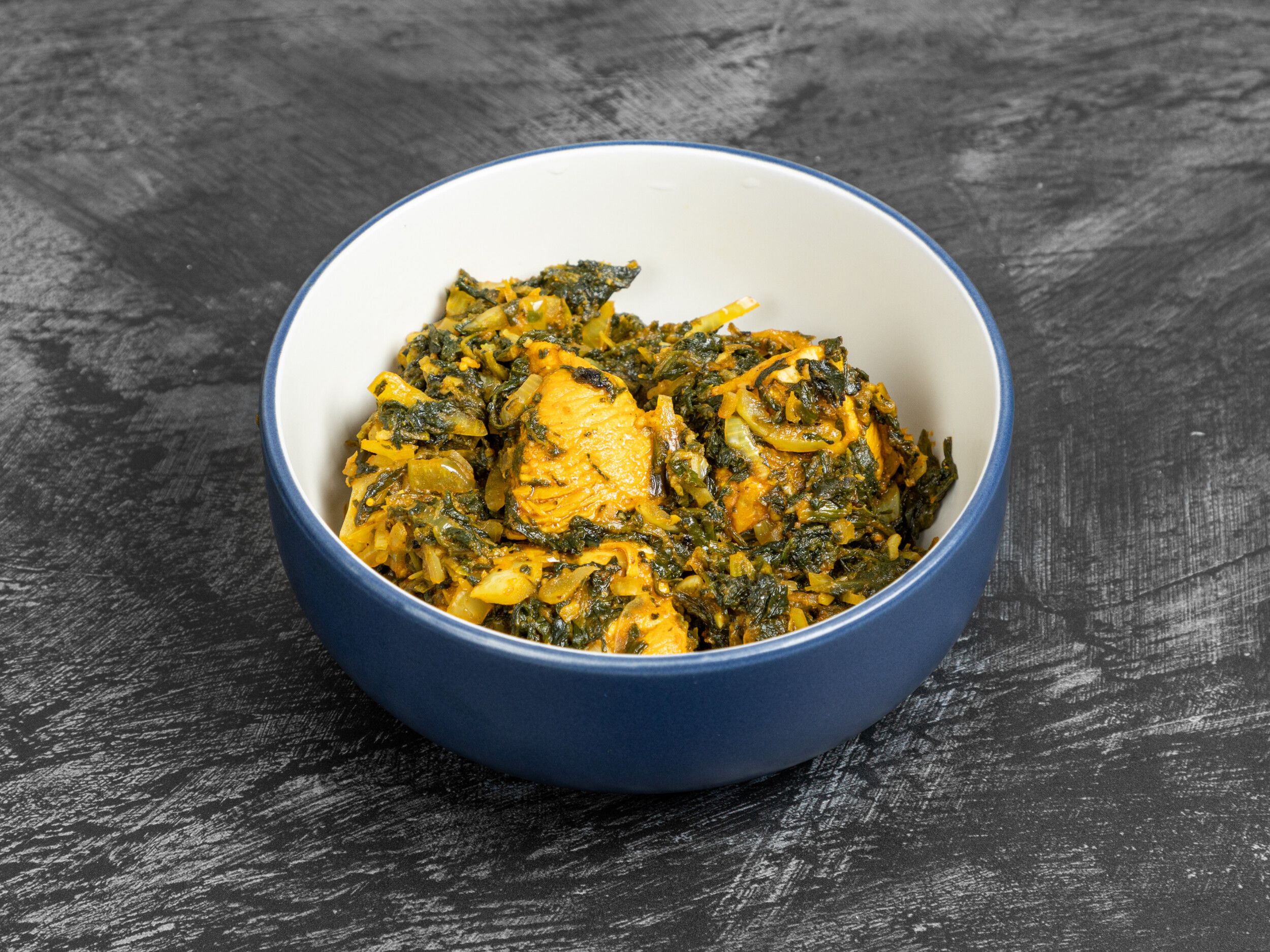 Korahi chicken with spinach and onions in a deep blue-rimmed white bowl on a dark grey surface