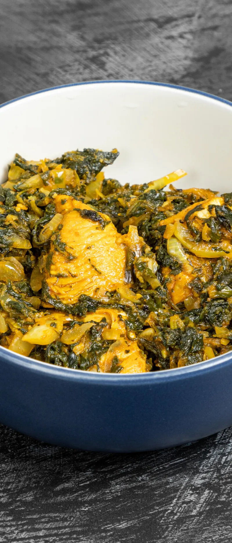 Korahi chicken with spinach and onions in a deep blue-rimmed white bowl on a dark grey surface