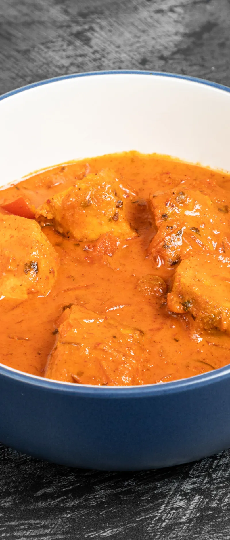 A blue and white bowl containing a vibrant orange chicken tikka masala curry with visible chicken pieces and tomato.