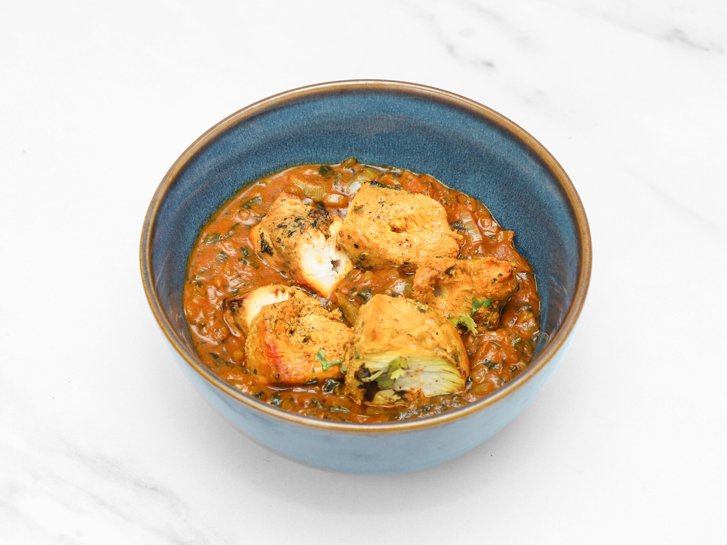 Several pieces of paneer submerged in a rich orange-red masala sauce with visible green herbs, served in a blue bowl.