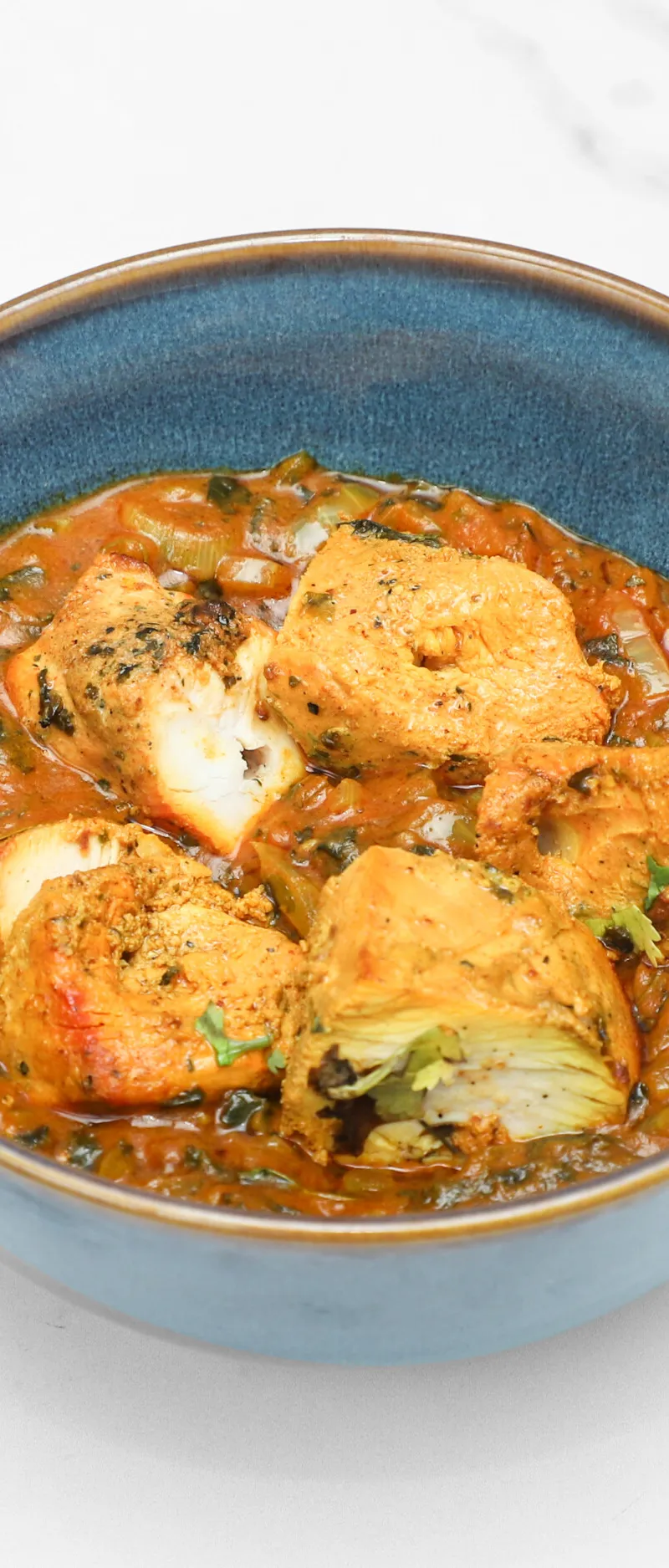 Several pieces of paneer submerged in a rich orange-red masala sauce with visible green herbs, served in a blue bowl.