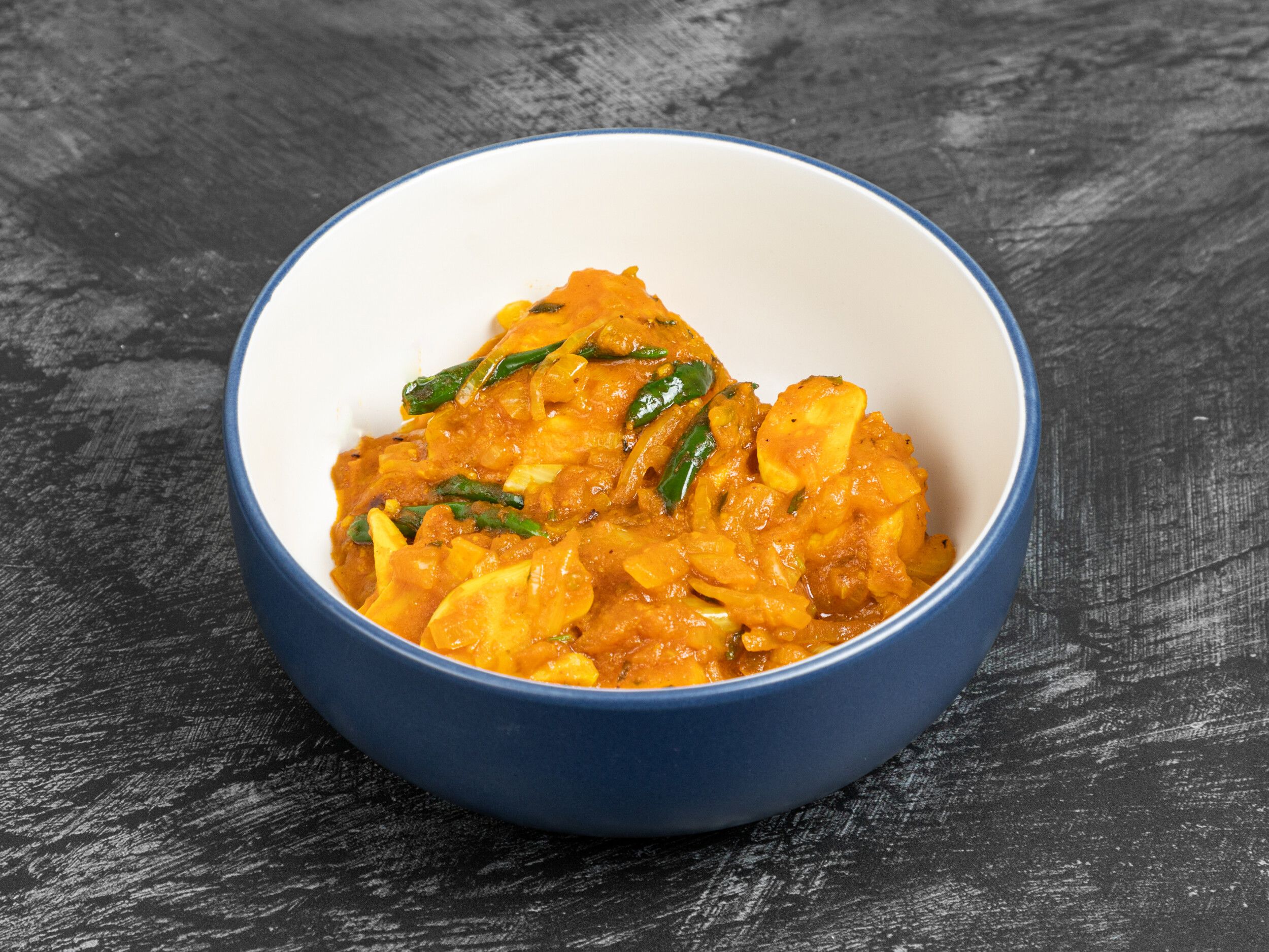 Aloo shim, an Indian potato dish in an orange sauce with sliced green chillies, served in a blue bowl with a white rim