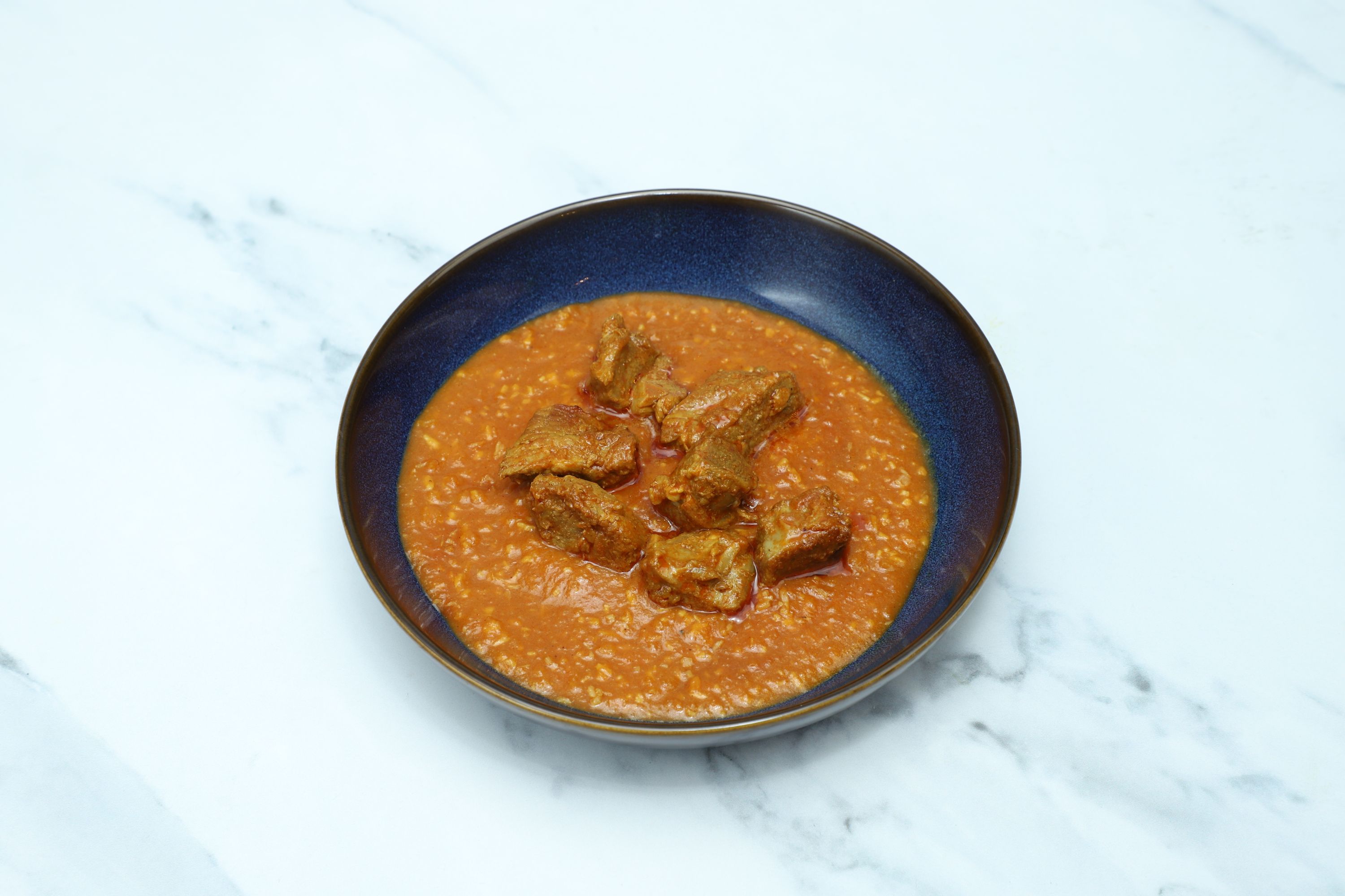 Hearty lamb curry with tender meat chunks in a rich orange sauce, served in a dark blue bowl.