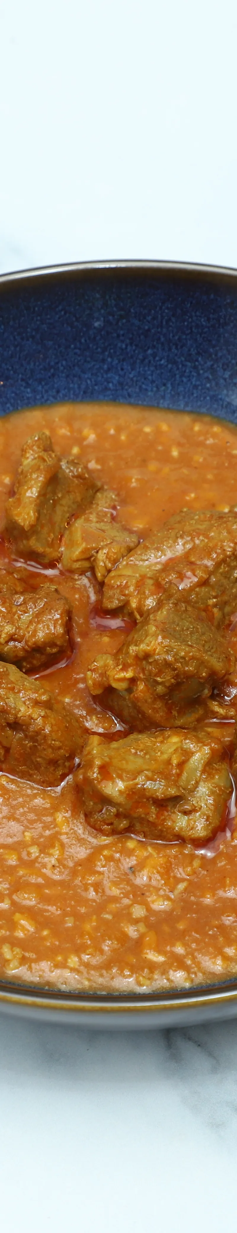 Hearty lamb curry with tender meat chunks in a rich orange sauce, served in a dark blue bowl.