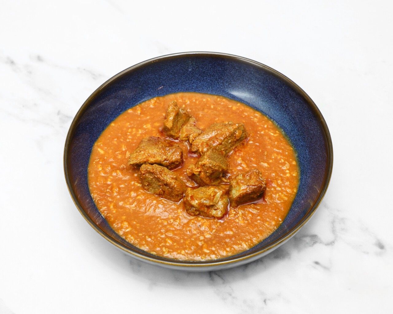 Lamb karahi curry with chunks of meat in a rich orange sauce, served in a dark blue bowl.