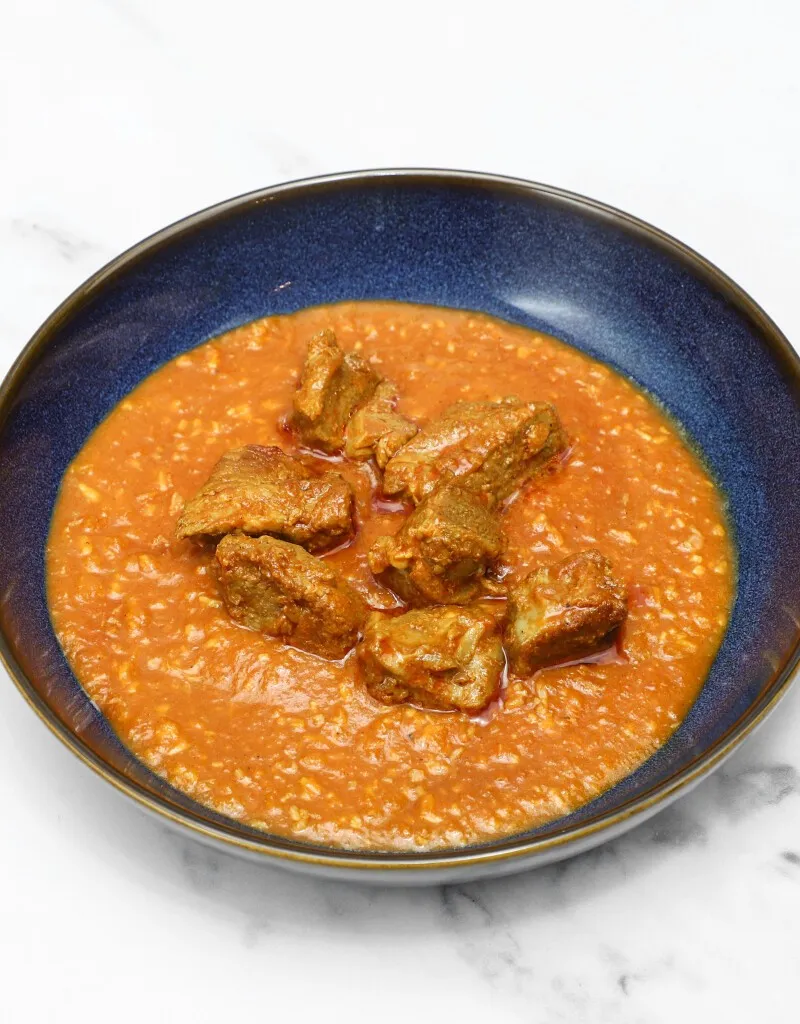 Lamb karahi curry with chunks of meat in a rich orange sauce, served in a dark blue bowl.