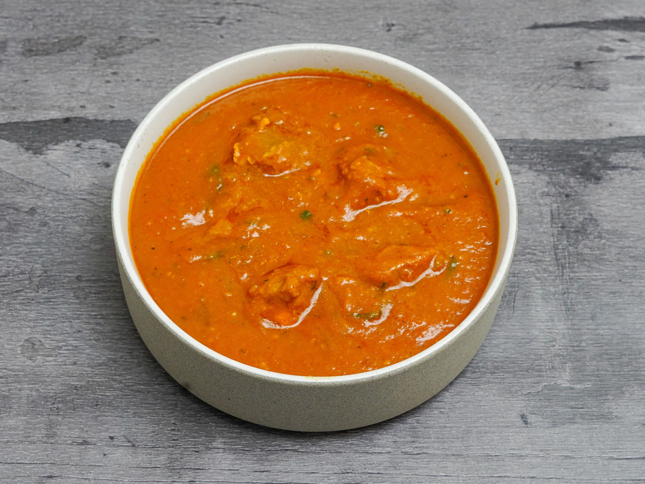 Orange karahi chicken curry in a white bowl, against a grey wooden background.