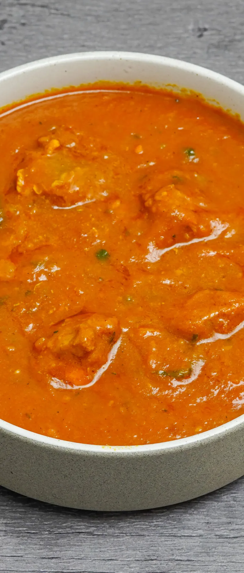 Orange karahi chicken curry in a white bowl, against a grey wooden background.